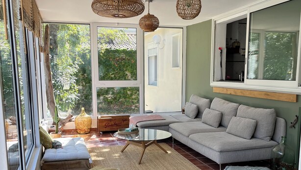 Ein geräumiges Wohnzimmer mit großem Fenster, einem grauen Sofa, einem Couchtisch und gewebten Teppichen.