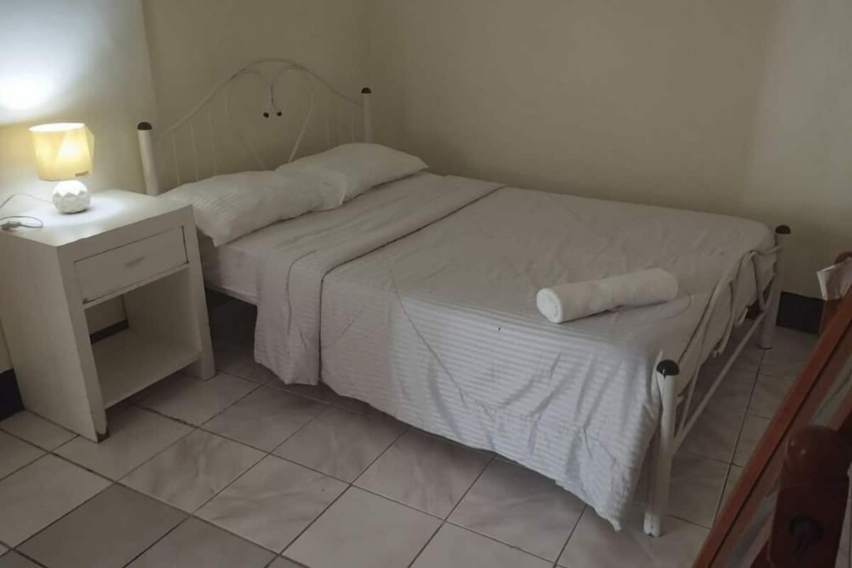 Une chambre avec un lit simple, un chevet avec une lampe et une commode en bois.