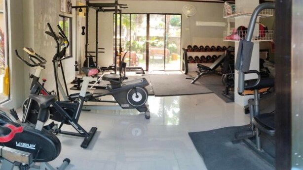 A gym with various exercise equipment, including treadmills and weight machines, and a wall of dumbbells. - Tayud Hotel by Hiverooms (Liloan)