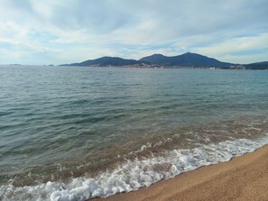 A beach with clear water, a sandy shore, and a distant cityscape with mountains. - Magnificent apartment 2 minutes walk from the beach and shops (Grosseto-Prugna)