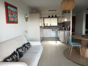 A modern kitchen with white cabinets, a dining area with a round table, and a living room with a sofa and decorative pillows. - Magnificent apartment 2 minutes walk from the beach and shops (Grosseto-Prugna)