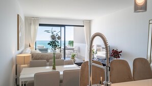 Ett modernt hotellrum med en matplats, ett stort fönster med utsikt över havet, en unik, böjd kran och en vas med blommor.