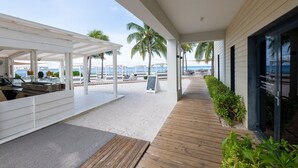 A beachside walkway with a covered seating area, palm trees, and a view of the ocean. - Luxurious Apartment in Jan Thiel with Pool (Jan Thiel)