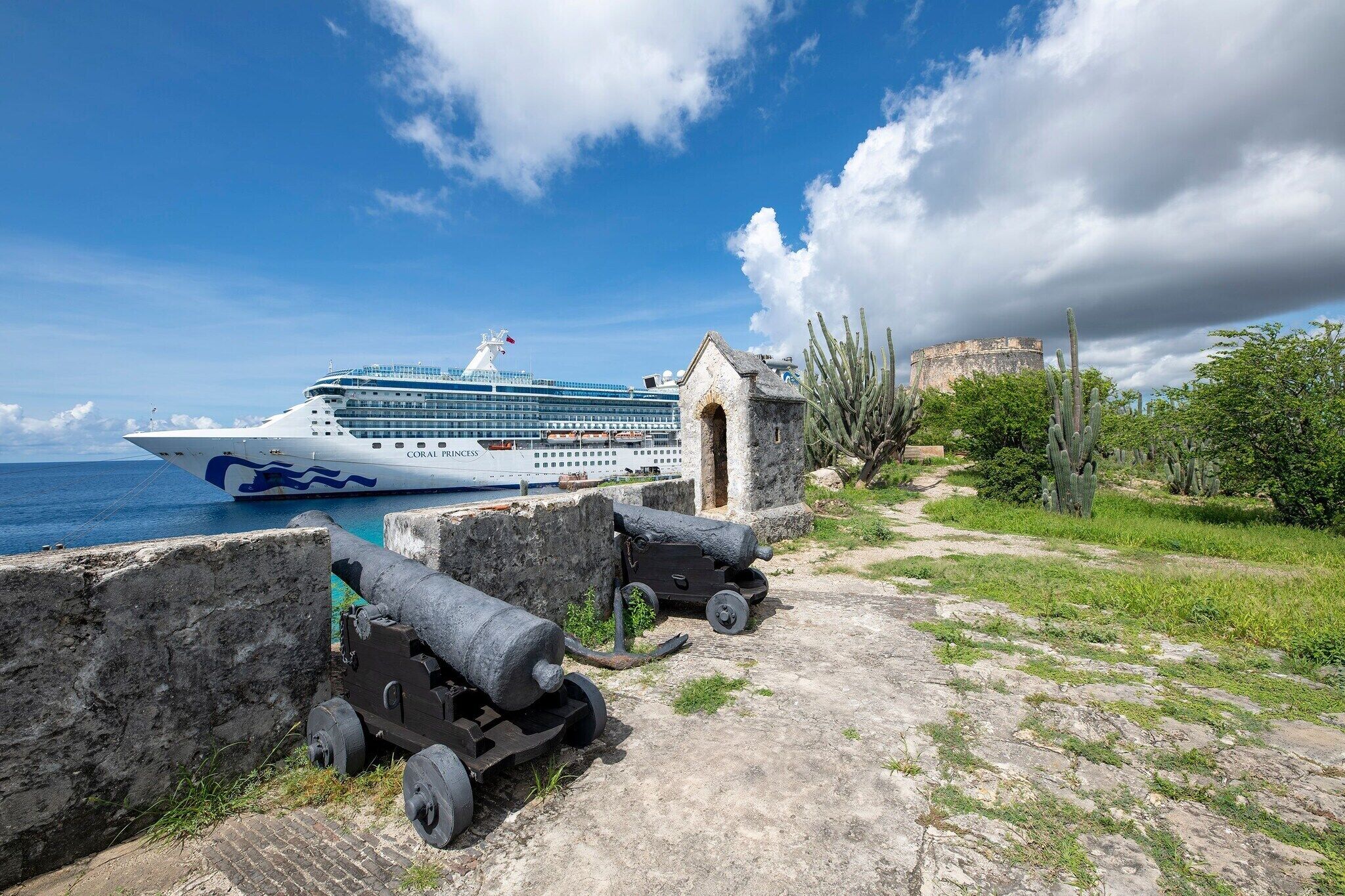 Un crucero amarrado en un puerto con cañones y un edificio histórico al fondo.