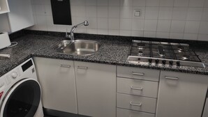 Una cocina con un lavamanos de acero inoxidable, una estufa a gas, una lavadora y armarios blancos.