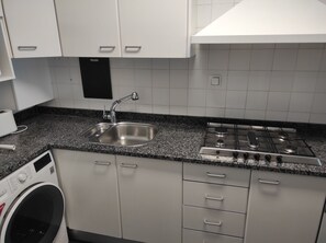 A kitchen with a stainless steel sink, a gas stove, a washing machine, and white cabinets. - Duplex with sea views (Pineda de Mar)