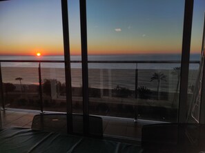Un balcón con vistas a la puesta de sol sobre el océano, con palmeras y cielo despejado.