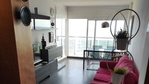 Una sala de estar moderna con un sofá rojo, un comedor con mesa de vidrio y ventanas amplias con vista al mar.