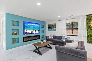 Una sala de estar moderna con una pared de acento color turquesa, un televisor de pantalla plana, un sofá gris y una mesa de centro.