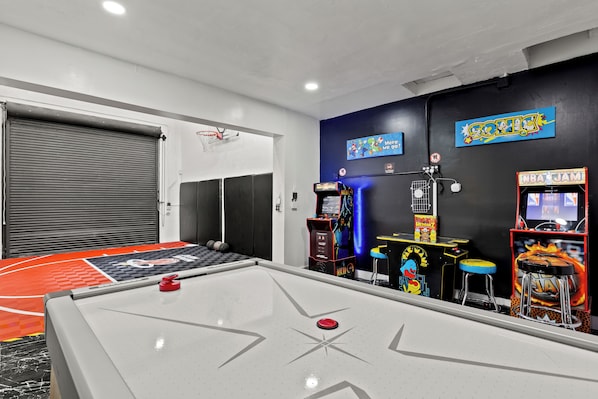 Una habitación con mesa de juego de losas, juegos de arcade y aro de baloncesto.