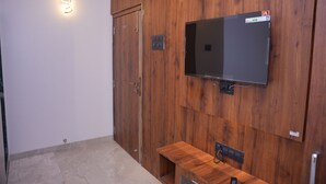 A room with a wooden panel wall, a flat-screen TV mounted above a wooden cabinet, and a door with a handle. - Venkat's The MOUNTAIN by Redwings (Khalapur)