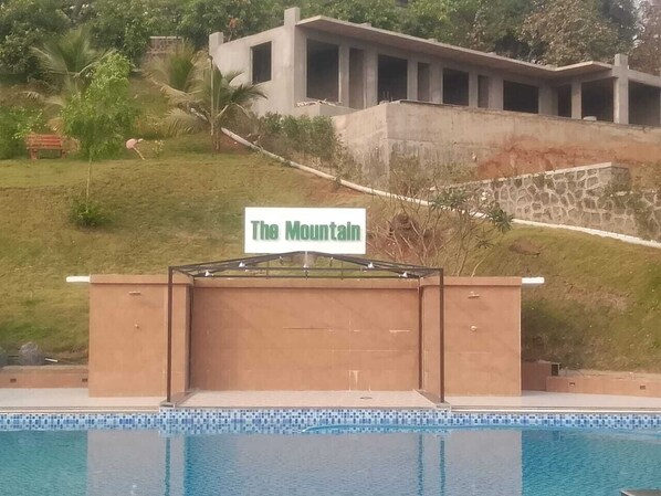 Een bord met de tekst 'The Mountain' boven een zwembadgedeelte met een modern gebouw op de achtergrond.