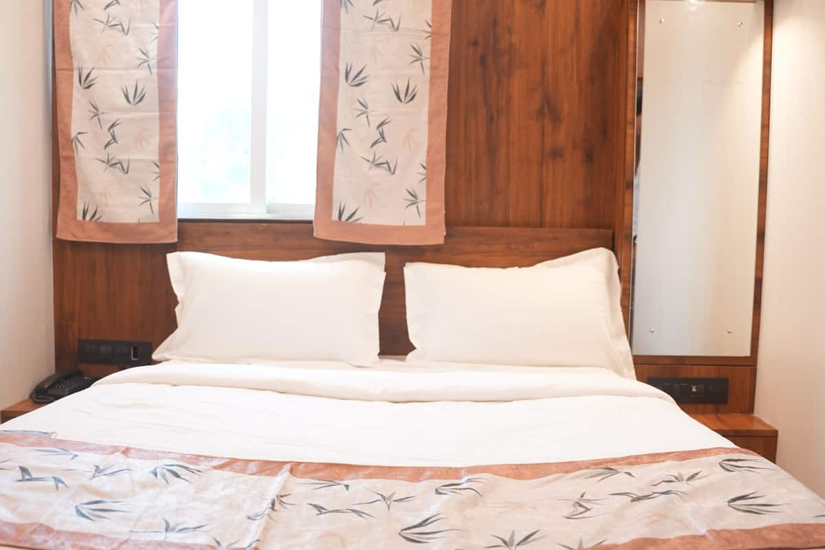 Un lit bien fait, avec du linge de lit blanc et un couvre-lit décoratif, une tête de lit en bois et un grand miroir au mur.