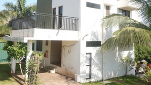 A two-story building with a balcony, a satellite dish, and a small garden area with palm trees. - Venkat's The MOUNTAIN by Redwings (Khalapur)