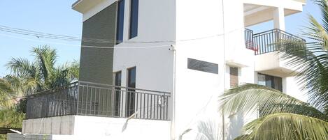 A two-story building with a balcony, a satellite dish, and a small garden area with palm trees.