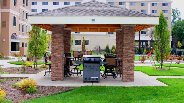 Un espacio de estar al aire libre techado con pilares de ladrillo, una parrilla y mobiliario exterior.