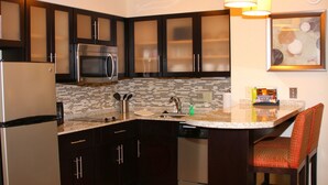 Una cocina moderna con armarios oscuros, electrodomésticos de acero inoxidable, salpicadero de azulejos y una barra con una silla.