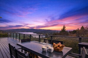 Una terraza con una mesa lista para el desayuno, con vista a un lago y montañas al atardecer.