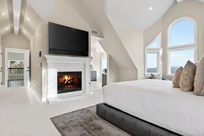 Un dormitorio amplio con una cama grande, una chimenea, un televisor montado encima y vistas amplias a través de ventanas grandes.