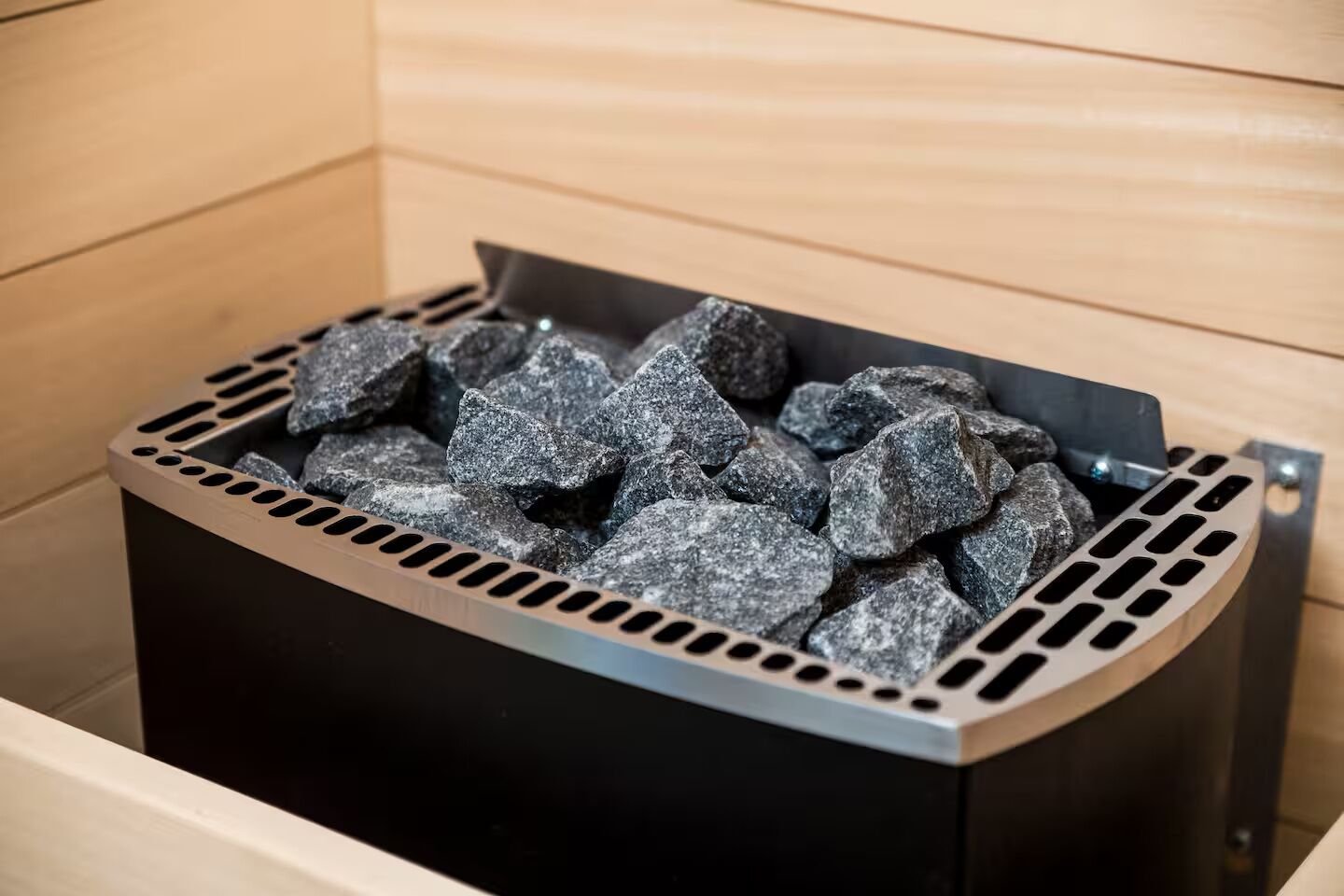 A black metal container filled with gray rocks, likely for a sauna or hot tub, in a wooden room.