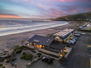 A coastal hotel with a parking lot, a beach view, and a pier in the background. - Oceanfront Cayucos Home + On the Sand + Firepit + Views + Steps to Cayucos Pier (Cayucos)