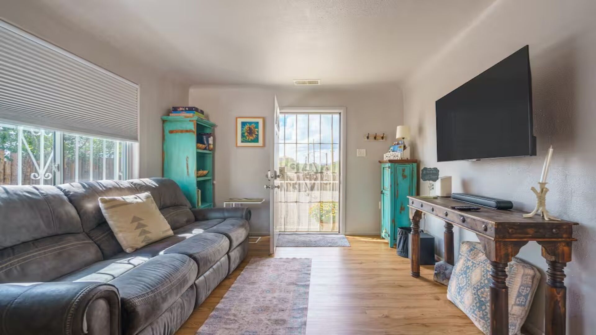 A living room with a grey sofa, a teal cabinet, a wooden table, and a TV mounted on the wall.