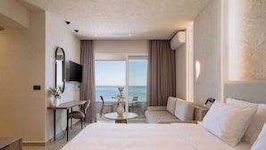 Een hotelkamer met een groot bed, een bureau met stoel, een kleine tafel, een bank, een televisie en uitzicht op zee.