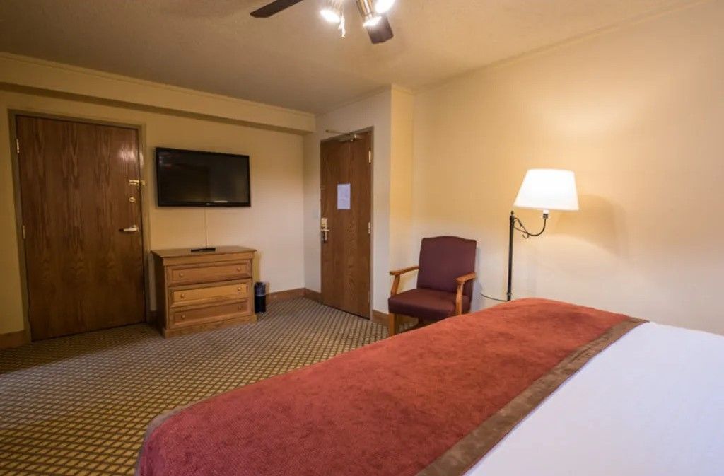 A hotel room with a bed, a dresser, a television, a chair, and a lamp.