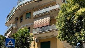 Un edificio residencial de varios pisos con balcones, una señal de paso para peatones y una entrada con portón.