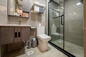Un baño moderno con cabina de ducha de vidrio, inodoro, lavabo con encimera de mármol y espejo sobre el lavabo.
