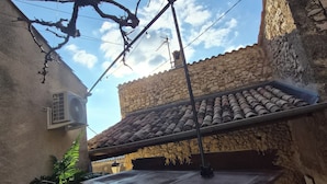 Un espace extérieur rustique, aménagé avec une table et des chaises en métal, entouré de murs en pierre et surmonté d’un toit en tuiles.