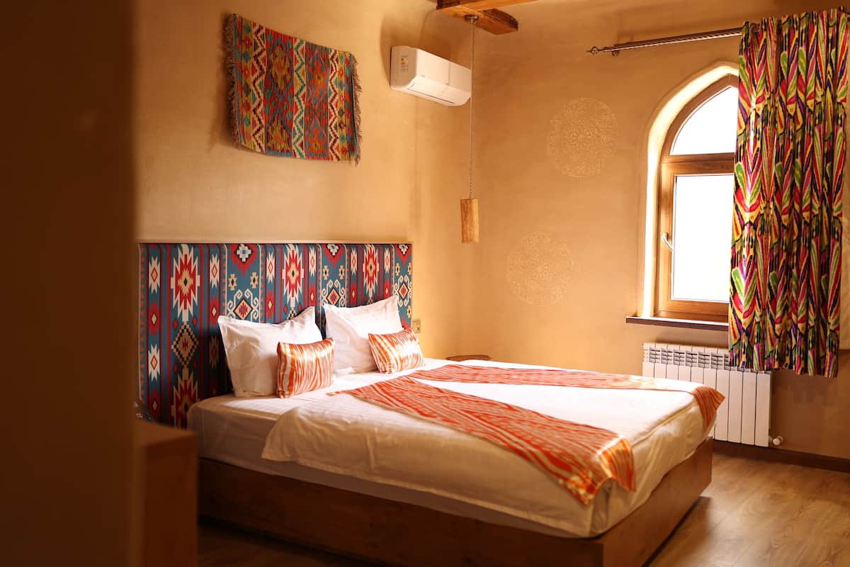 Une chambre à coucher avec un lit, des rideaux à motifs, un radiateur et une fenêtre.