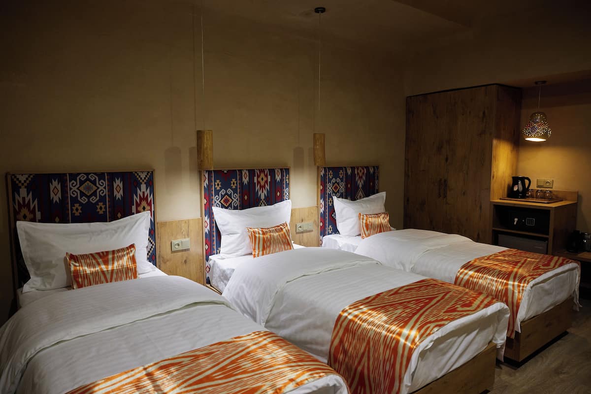 Une chambre d’hôtel avec trois lits, des têtes de lit en bois et une petite kitchenette.