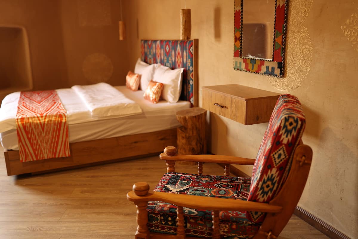 Un lit avec une tête de lit à motifs, une table de chevet en bois et une chaise avec un coussin coloré.