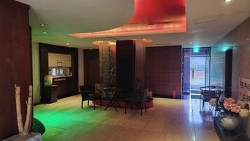 A lobby with a reception desk, seating area, and a large vase with flowers.