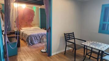 A bedroom with a bed, a chair, a table, and a fan.