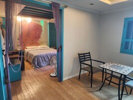 Un dormitorio con cama, una silla, una mesa y un ventilador.