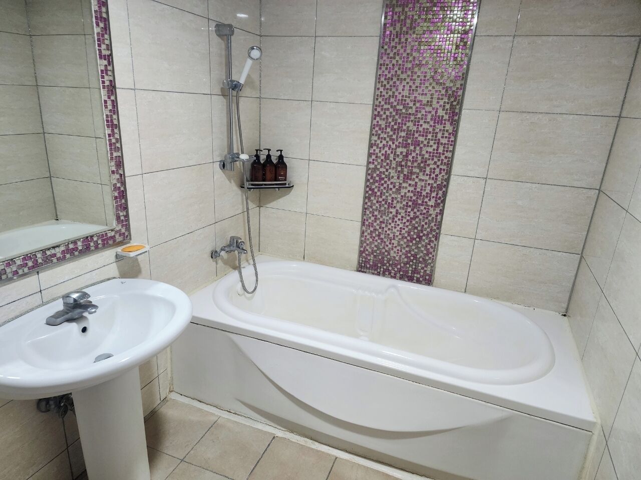 A bathroom with a white bathtub, a sink, and a shower. There are toiletries on a shelf.