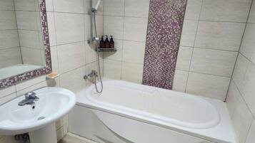 A bathroom with a white bathtub, a sink, and a shower. There are toiletries on a shelf.