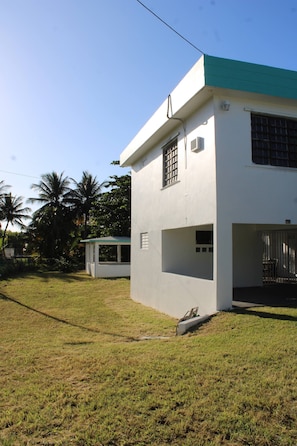 A white building with a green roof, a covered outdoor seating area, and a grassy yard.