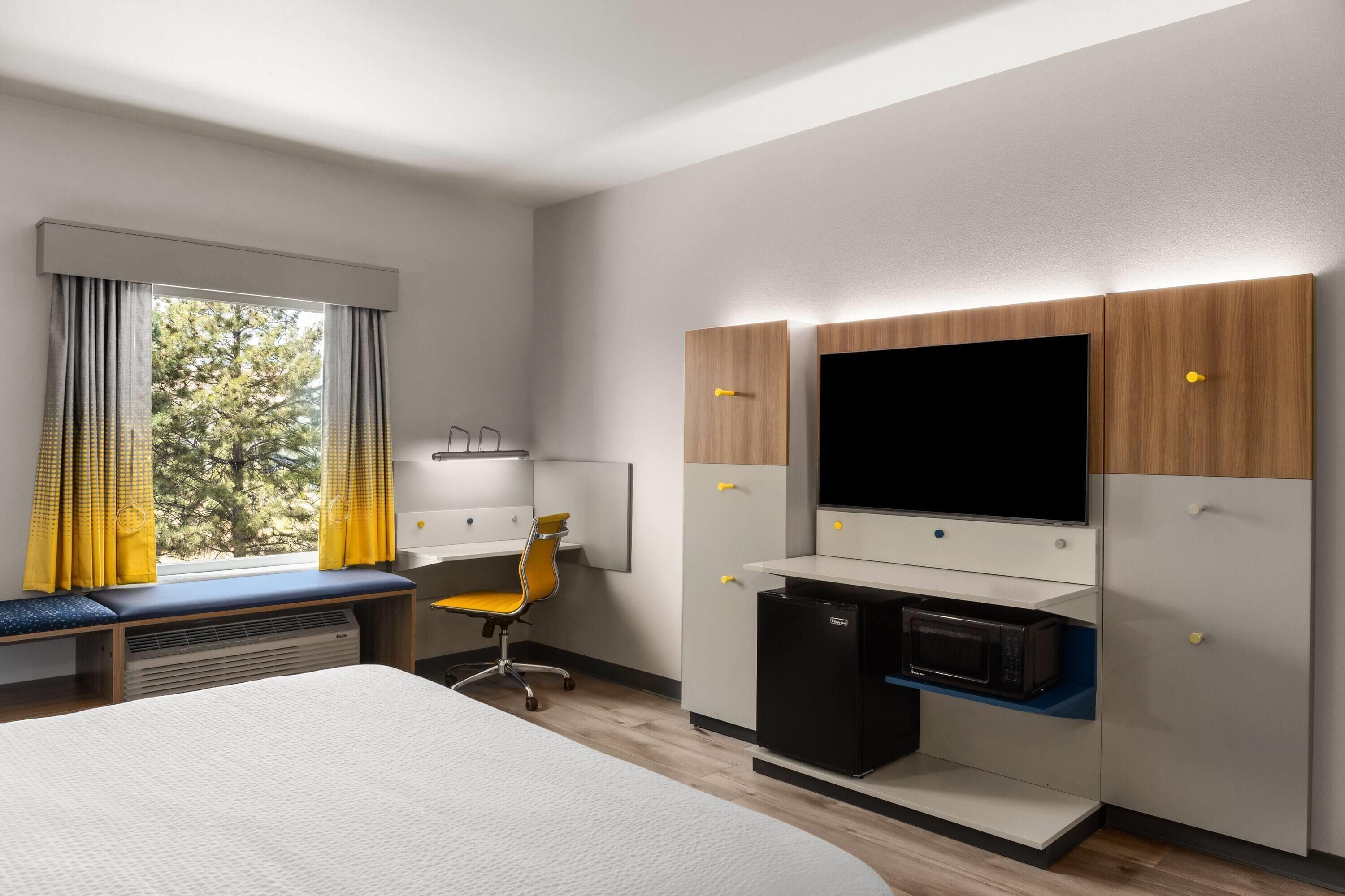 Una habitación de hotel con cama, escritorio, silla, televisor y minibar.