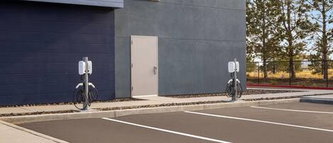A parking lot with two electric vehicle charging stations, a building with a grey facade, and a clear sky.