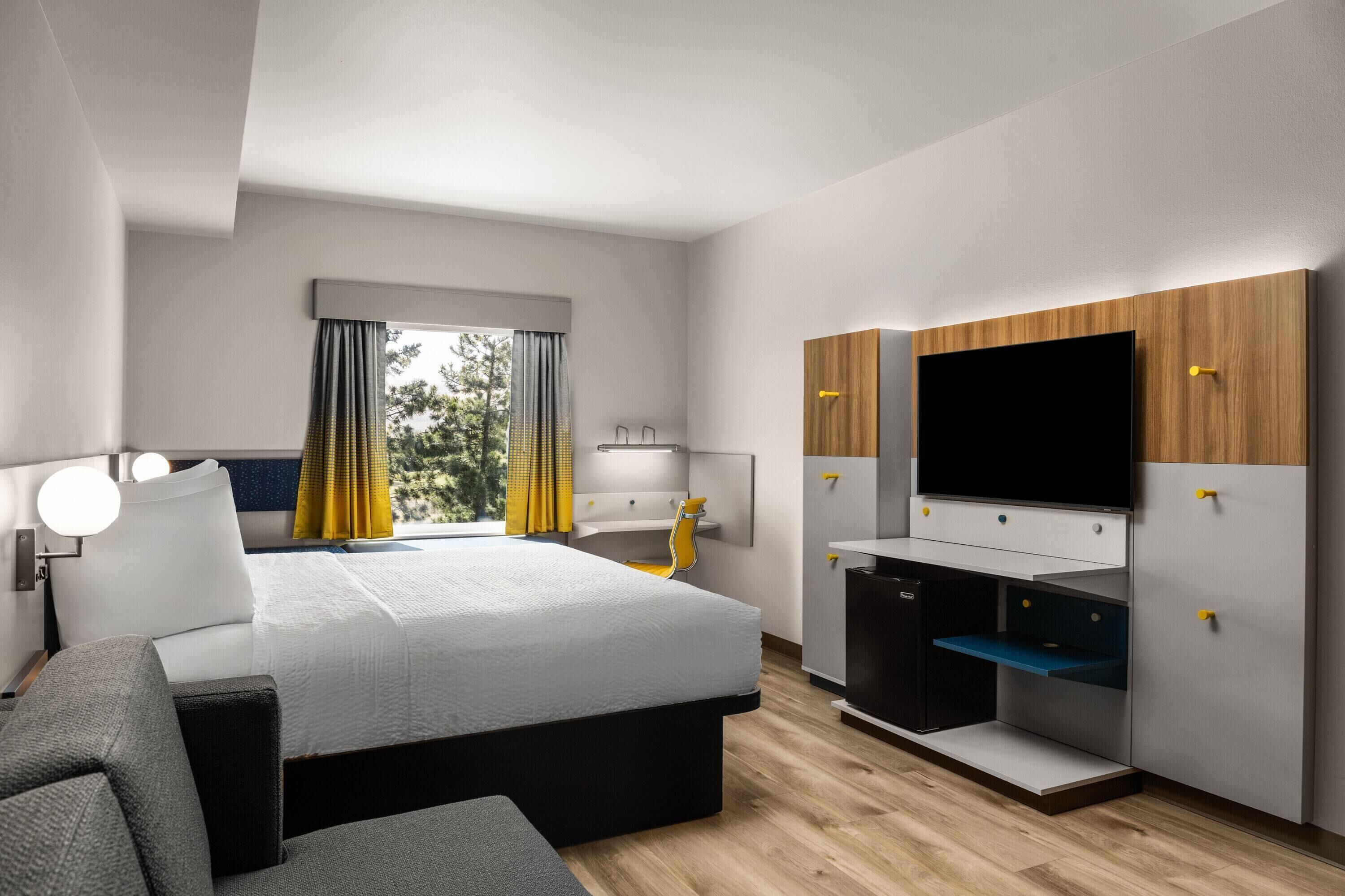 Moderni hotellihuone, jossa on sänky, työpöytä ja televisio.
