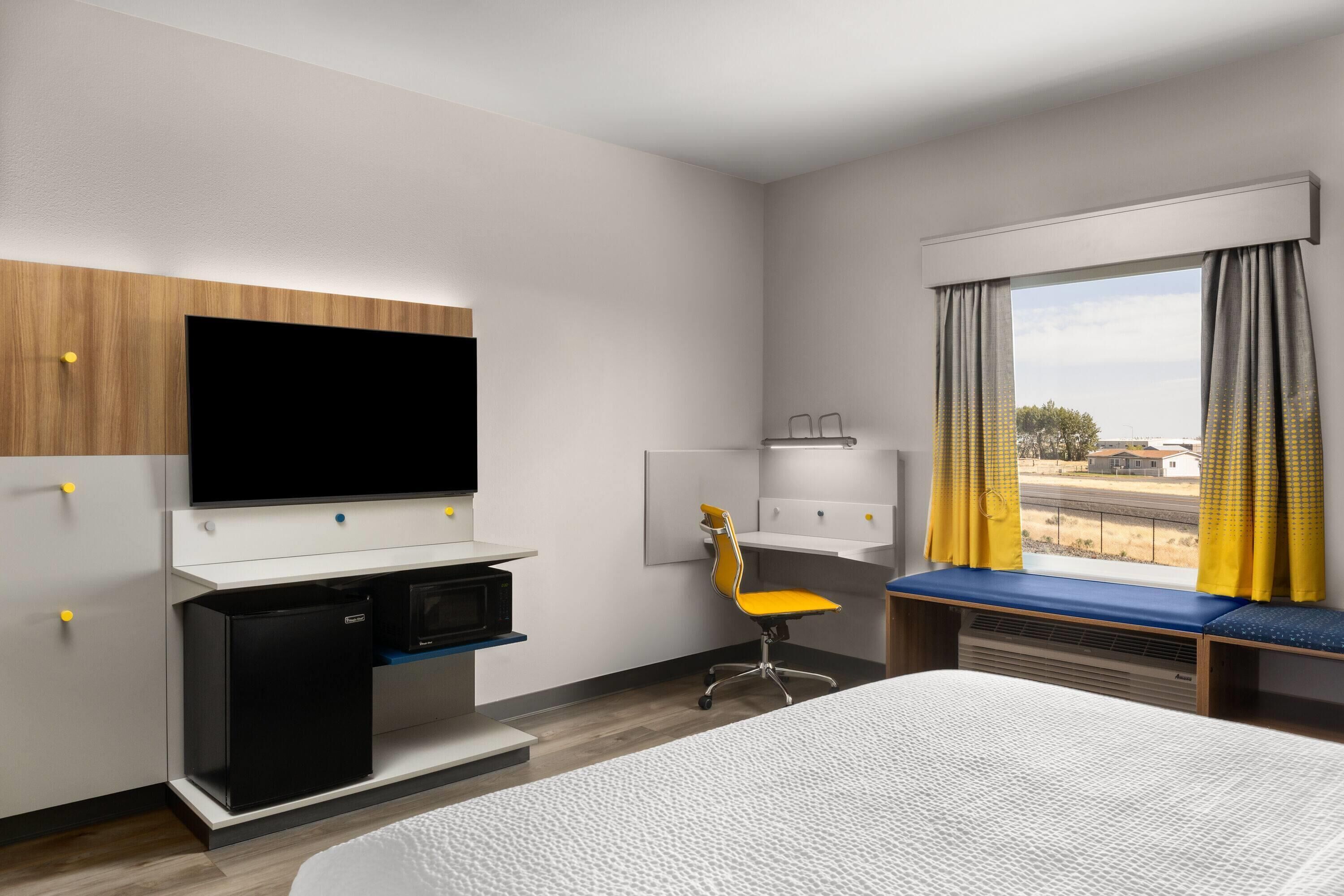 A hotel room with a bed, a desk with a computer, a television, a chair, and a window with curtains.
