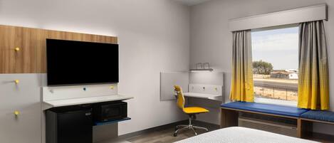 A hotel room with a bed, a desk with a computer, a television, a chair, and a window with curtains.