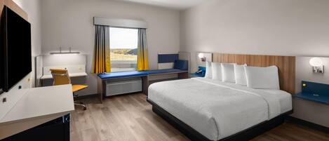 Une chambre d’hôtel avec un lit, un bureau, une chaise, une télévision et une fenêtre avec des rideaux.