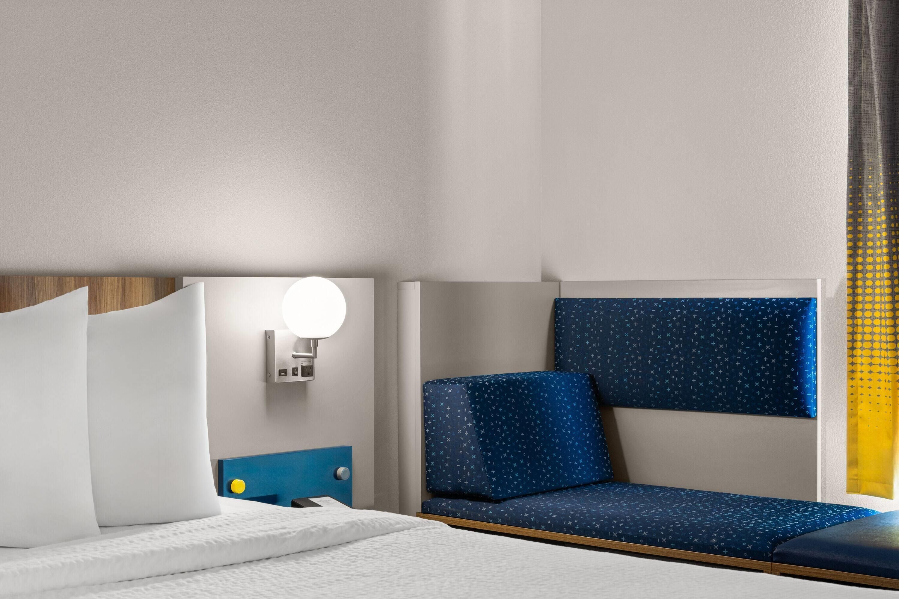 A hotel room with a bed, a bedside table, a lamp, and a window with curtains.