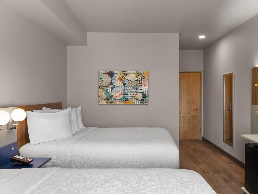 Una habitación de hotel moderna con una cama, una mesita de noche, una lámpara, un cuadro en la pared y un televisor.