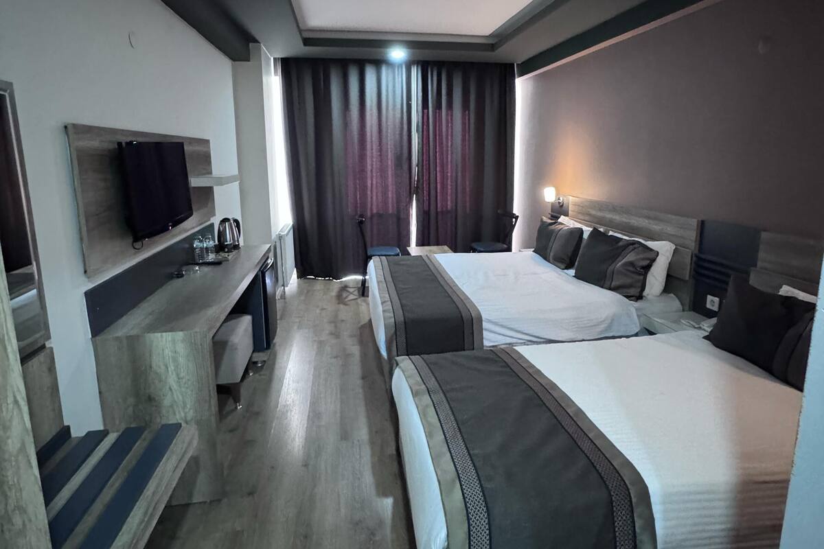 Een hotelkamer met twee bedden, een bureau met een flatscreen televisie, een zithoekje en een groot raam met gordijnen.