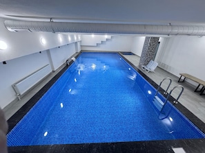 An indoor swimming pool with clear water, a black tiled edge, and a bench.